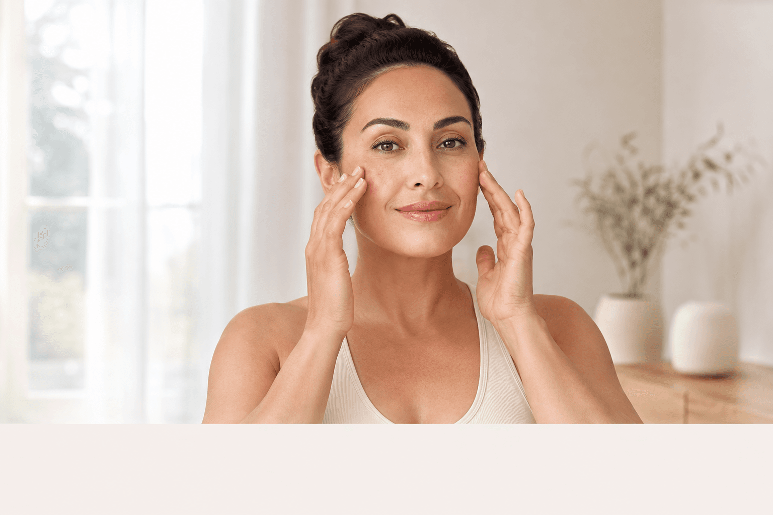 A brunette woman with her hair tied up gently practicing a facial massage